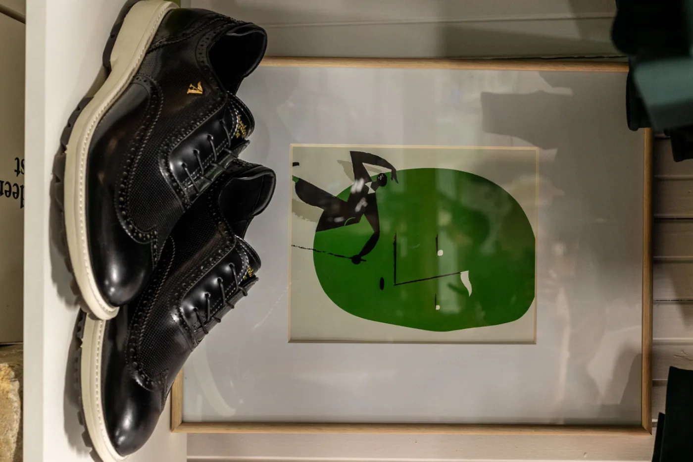 Black wingtip golf shoes on a shelf below a green golf print