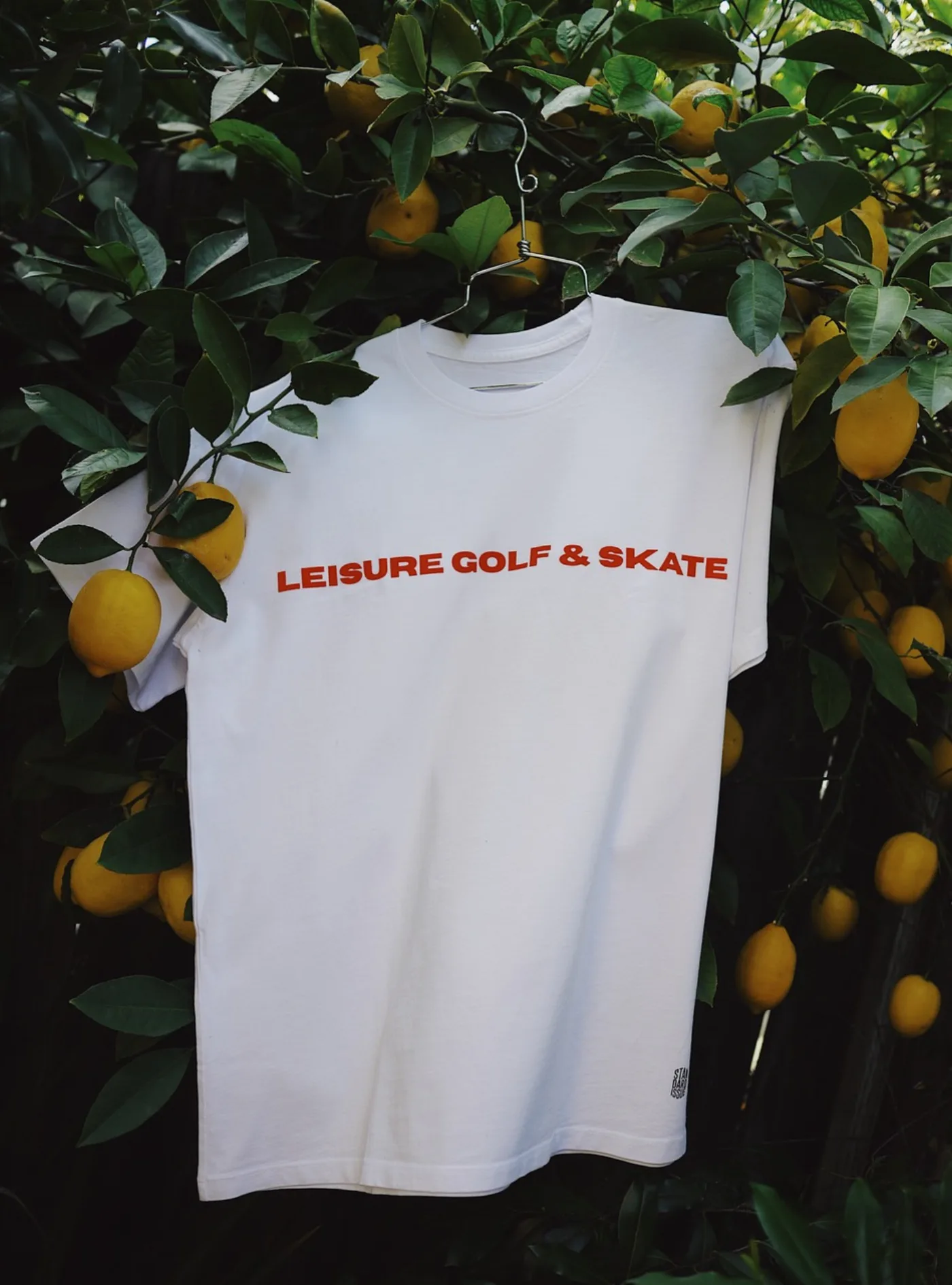 White Leisure Golf and Skate tee hanging in a lemon tree